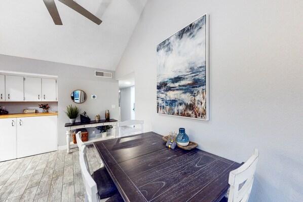 Un comedor moderno con una mesa de madera oscura, sillas blancas y un cuadro abstracto grande en la pared.