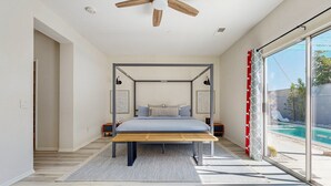 Een moderne slaapkamer met een hemelbed, een plafondventilator en uitzicht op een zwembad.