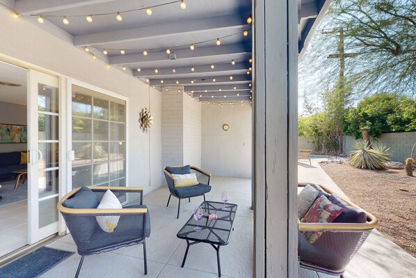 An outdoor patio with wicker furniture, a glass door entrance, and string lights. - Sun-soaked oasis with a pool, covered patio, grill, modern interior, W/D, & AC (Palm Springs)