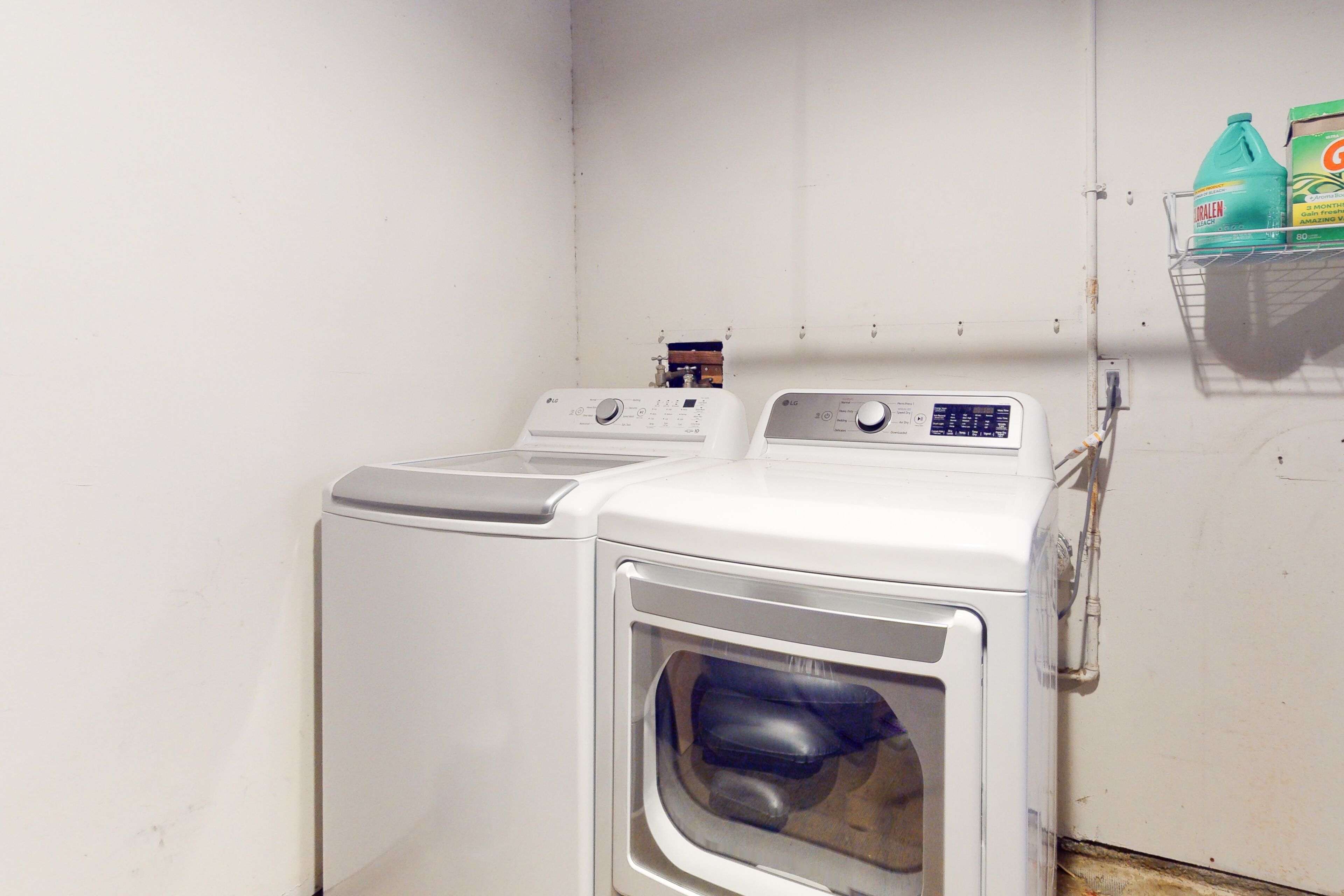 A laundry area with two washing machines and a shelf with detergent bottles.