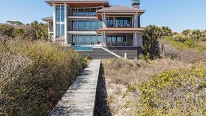 Una casa a più piani con un'ampia vetrata frontale, una piscina e un vialetto che conduce all'ingresso.