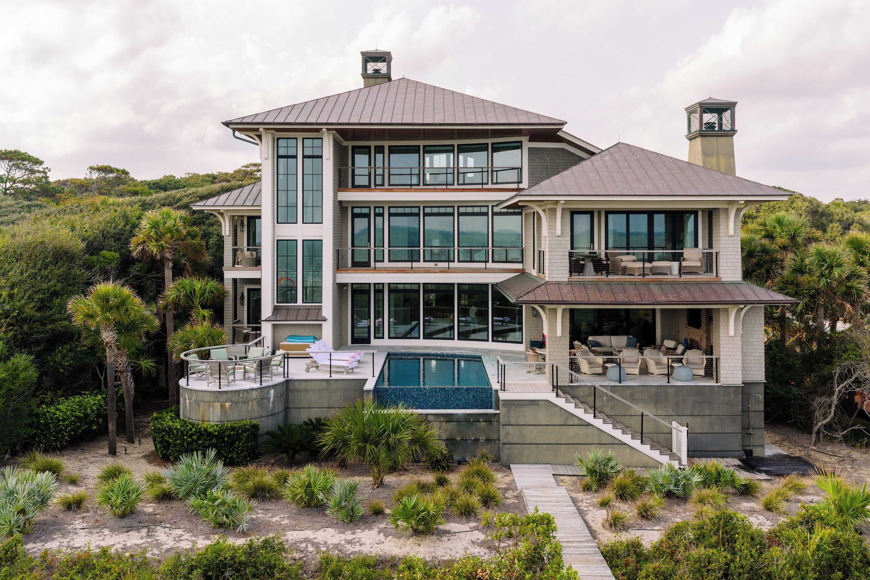 A modern two-story house with a large glass facade, a swimming pool, and a landscaped garden.