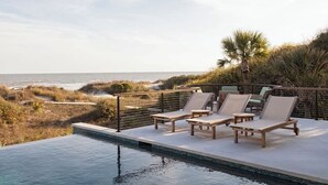 Area piscina con lettini, vista sull'oceano e paesaggio naturale.