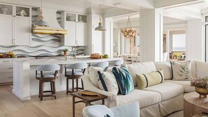Una cucina moderna con mobili bianchi, un'isola centrale, sgabelli da bar e un'area salotto con divano e poltrone.