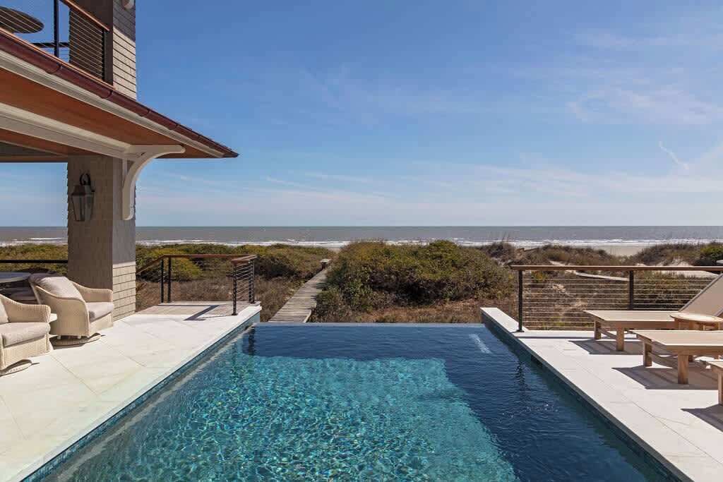 A pool with clear water, surrounded by lounge chairs and a view of the ocean.