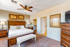 A bedroom with a wooden bed, two bedside tables with lamps, a ceiling fan, and a large mirror. - Open & bright condo with WiFi, W/D, pool, hot tub & panoramic views (Oro Valley)