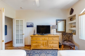 Ein Zimmer mit einem Fernsehschrank aus Holz, einem Fernseher, einem Sessel, einem Bett und einer Tür zu einem weiteren Raum.