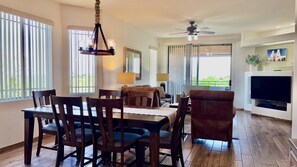 A dining area with a table and chairs, a ceiling fan, and a television in a living room. - Open & bright condo with WiFi, W/D, pool, hot tub & panoramic views (Oro Valley)