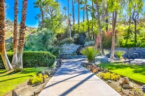 A pathway leading through a landscaped garden with various plants and a stone wall. - Dog-Friendly Modern Condo w/ Great Views, Shared Pool & Private Patio (Palm Springs)