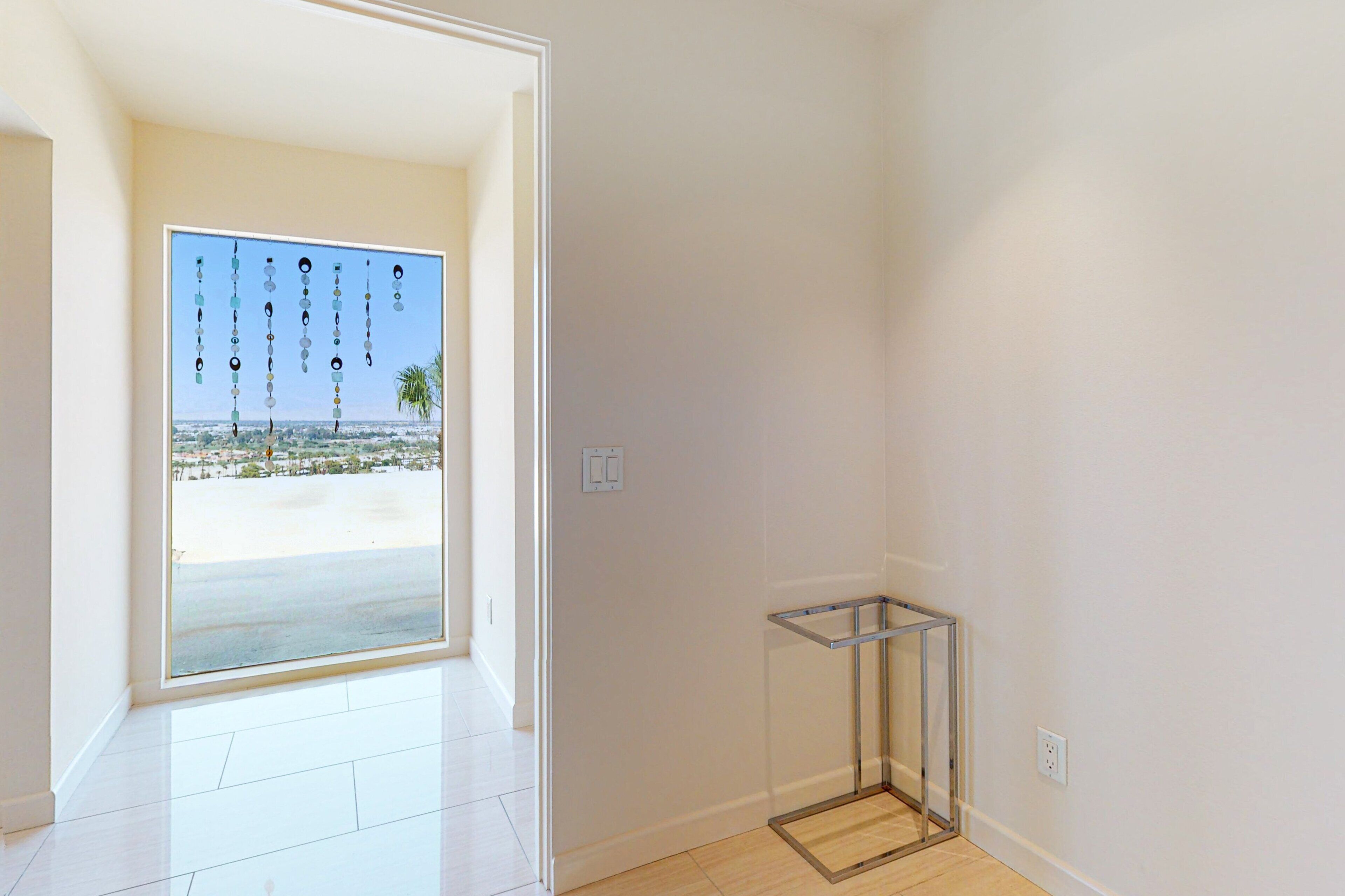 A room with a large glass door leading to a balcony with a view of a beach and palm trees.