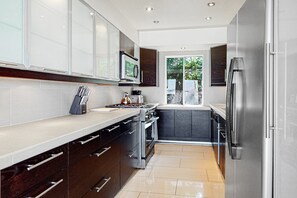 A modern kitchen with stainless steel appliances, dark cabinetry, and a large window providing natural light. - Dog-Friendly Modern Condo w/ Great Views, Shared Pool & Private Patio (Palm Springs)