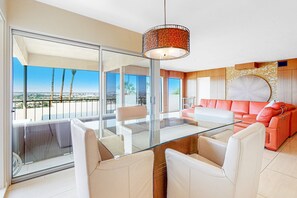 A modern living room with a glass table, leather chairs, a red sofa, and a view of the city. - Dog-Friendly Modern Condo w/ Great Views, Shared Pool & Private Patio (Palm Springs)