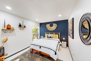 A bedroom with a bed, a bedside table, a wall-mounted mirror, and decorative items. - Dog-friendly home near Joshua Tree NP with Cowboy pool, mountain view, firepit (Joshua Tree)
