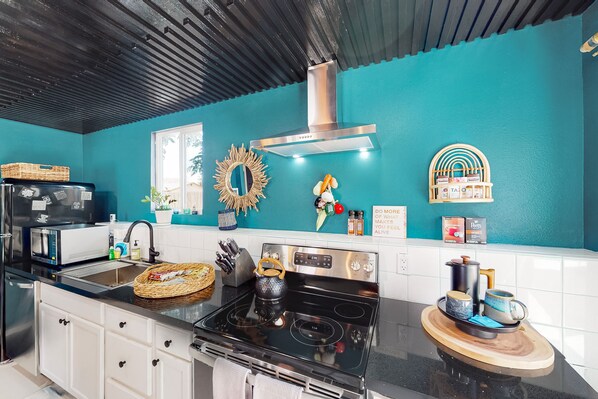 A kitchen with a black stove, white cabinets, a teal backsplash, and various kitchen items on the counter. - Dog-friendly home near Joshua Tree NP with Cowboy pool, mountain view, firepit (Joshua Tree)