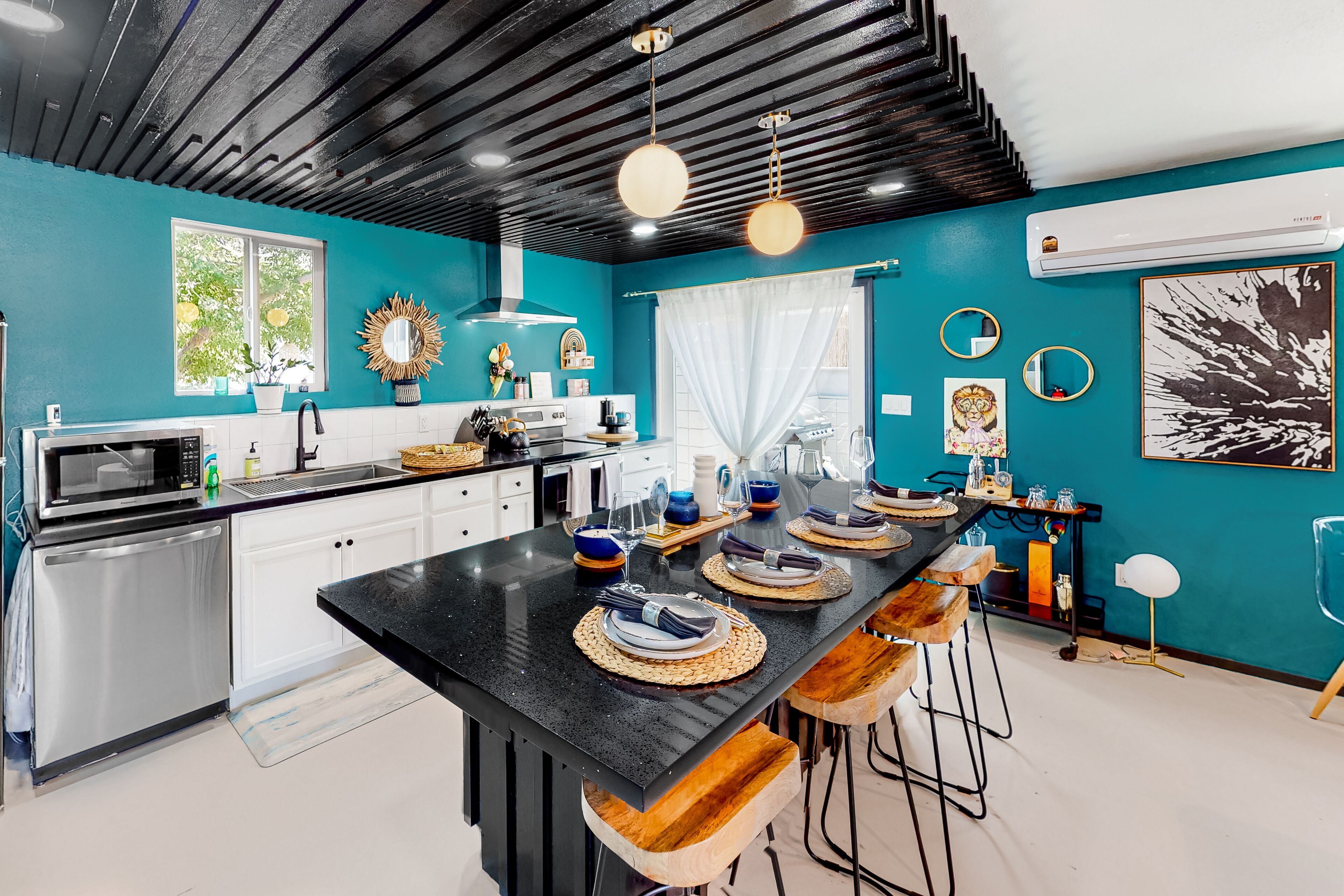 A modern kitchen with a central island, stainless steel appliances, and teal walls.