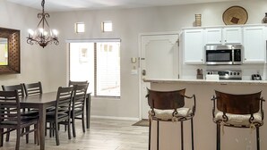 Een moderne keuken met witte kasten, roestvrijstalen apparatuur en een eethoek met houten stoelen en een kroonluchter.