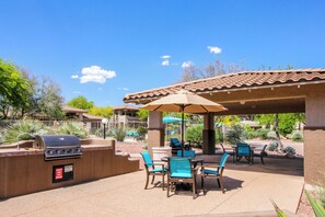 Eine Terrassengruppe draußen mit Grill, Stühlen und Tisch unter einer Pergola.