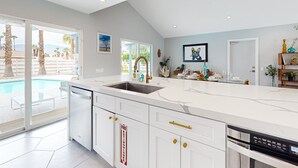 Una cocina moderna con una isla grande, armarios blancos y vistas a una piscina.