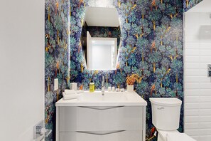 A bathroom with a white sink, mirror, and toilet. The walls are decorated with a tropical leaf pattern. - Mid-century modern hacienda with pool, outdoor kitchen, & fireplace - dogs ok (Palm Springs)