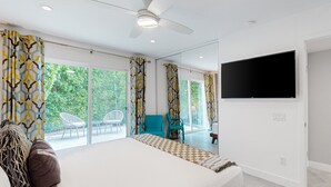 Un dormitorio moderno con una cama grande, ventilador de techo, televisión y balcón con sillas.