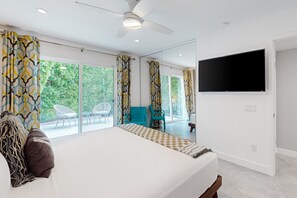 A modern bedroom with a large bed, a ceiling fan, a TV, and a balcony with chairs. - Mid-century modern hacienda with pool, outdoor kitchen, & fireplace - dogs ok (Palm Springs)