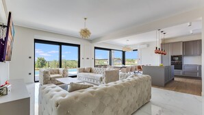A modern living room with a large beige sofa, a dining area, and a kitchen with grey cabinets. - Stunning home in Galilzana (Galilzana)