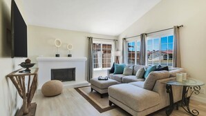 Un salon moderne avec un canapé, un pouf, une cheminée et un téléviseur fixé au mur.