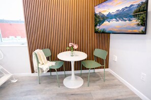 A room with a round white table, two green chairs, a vase with flowers, and a wooden slatted wall. - Walk to Yale | King Loft & Queen Bedroom (New Haven)