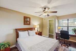 Une chambre à coucher comprenant un lit, un bureau, une chaise, un ventilateur de plafond, une fenêtre et une porte.