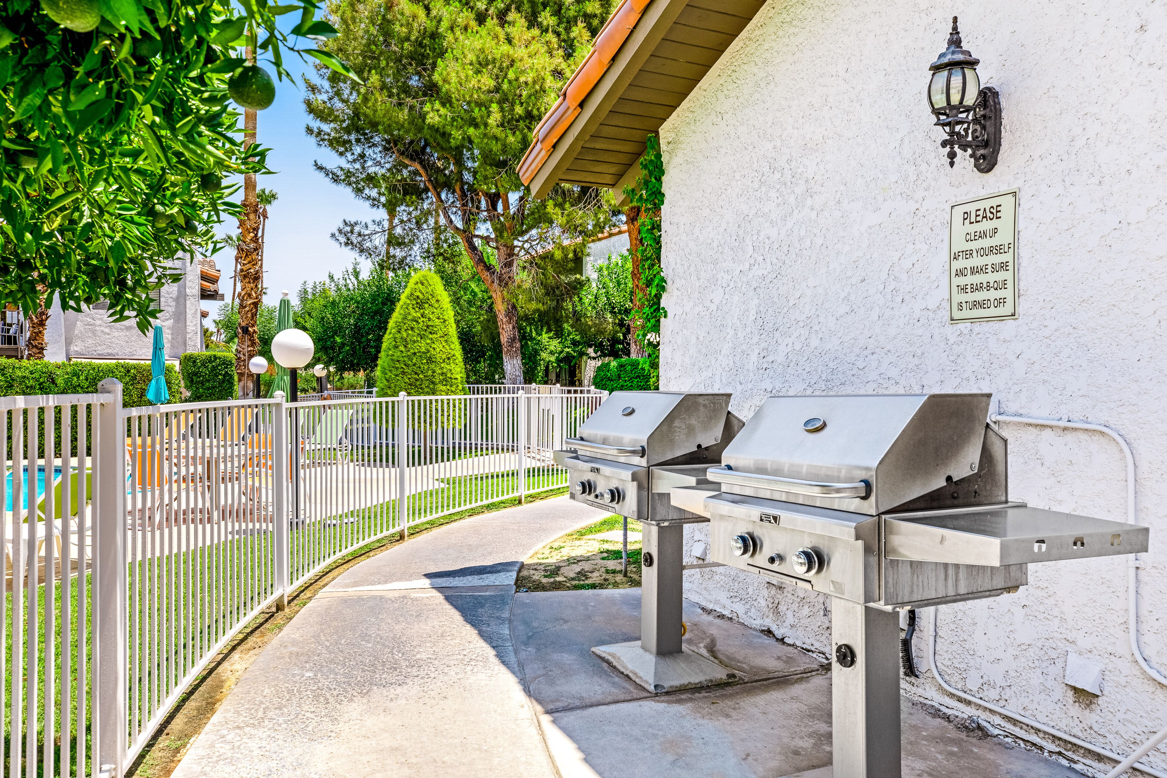 An outdoor barbecue area with a grill, a fence, and a sign on the wall.