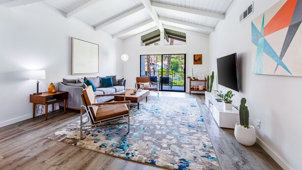 Een ruime woonkamer met een hoge plafond, groot raam, flatscreen televisie en een moderne bank.