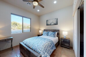 A bedroom with a bed, a desk, a window, a ceiling fan, and a nightstand with a lamp. - Updated home with mountain views, a private patio, grill, EV charger, W/D, & AC (Tucson)