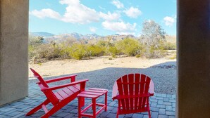 Eine Terrasse mit zwei roten Adirondack-Stühlen und einem kleinen Tisch, mit Blick auf eine Wüstenlandschaft mit Bergen im Hintergrund.