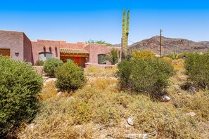 Ein gebäude im Wüstenstil mit flachem Dach und Stuckwänden, umgeben von trockener Vegetation und einem Berg im Hintergrund.