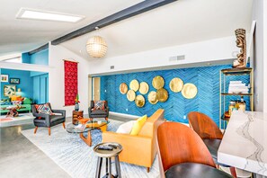 Ein modernes Wohnzimmer mit blauer Fischgrätwand, einem runden Couchtisch und einer Couch mit orangenen Kissen.