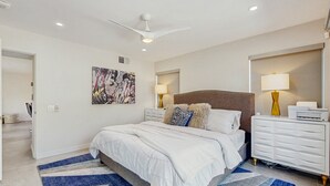 Una camera da letto moderna con un letto grande, comodini bianchi, una ventola a soffitto e una TV a parete.