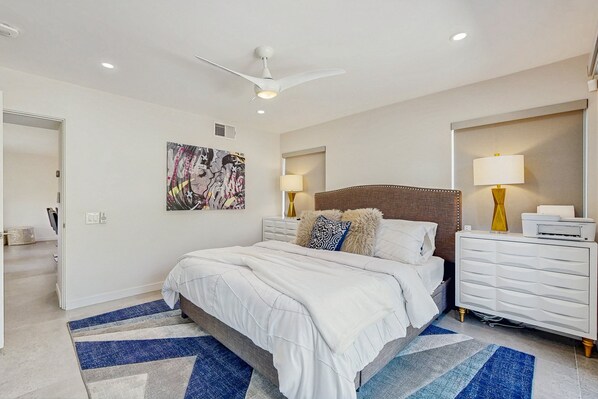 A modern bedroom with a large bed, white nightstands, a ceiling fan, and a wall-mounted TV. - Relax, dine, and explore with ease soak up the sunshine. Home is Dog Friendly. (Palm Springs)