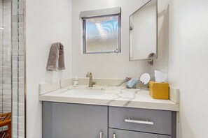 A bathroom with a marble sink, a towel hanging on the wall, a window with a textured pattern, and a mirror. - Relax, dine, and explore with ease soak up the sunshine. Home is Dog Friendly. (Palm Springs)