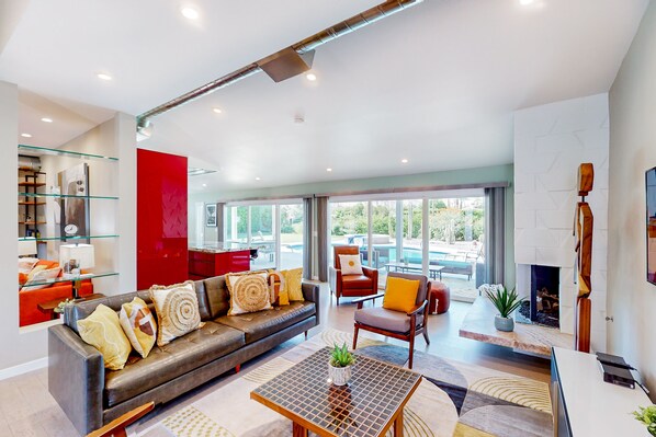 Una sala de estar moderna con sofá de cuero, estanterías de vidrio, chimenea y vistas al exterior.