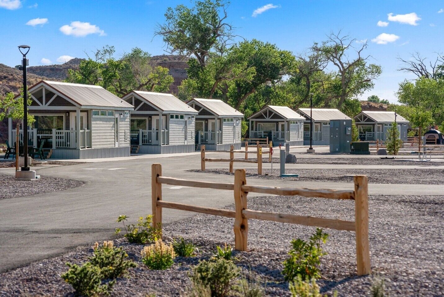 A row of cabins with a gravel driveway and wooden fence in the foreground.
