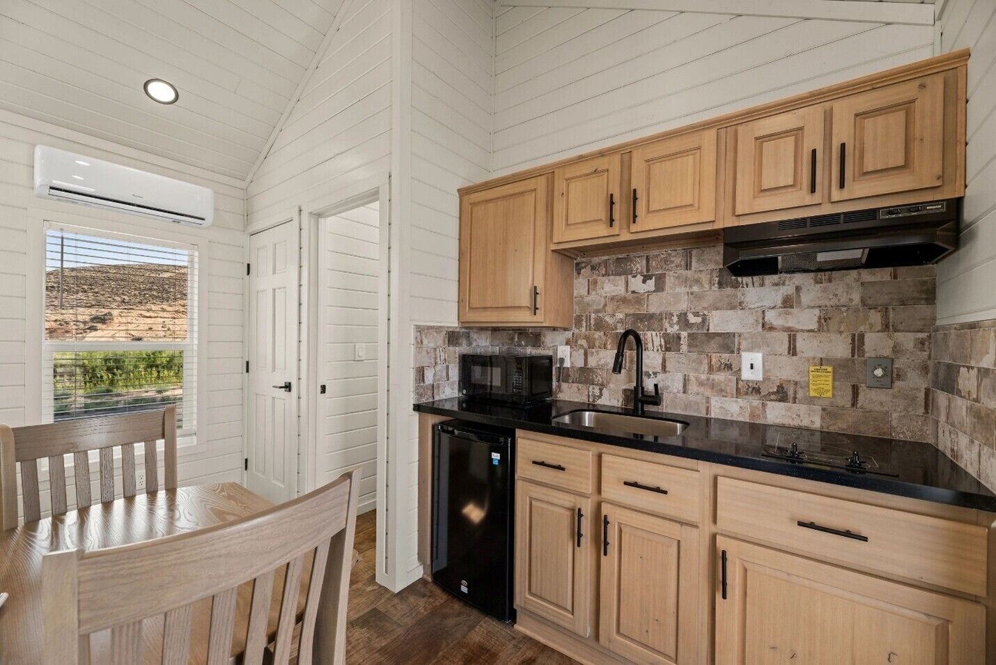 A kitchen with wooden cabinets, a black dishwasher, and a stone backsplash.