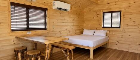 Una habitación de cabaña de madera con una cama, una mesa y dos ventanas.