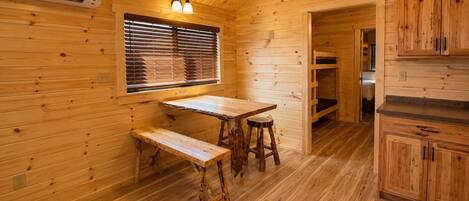 A wooden interior with a table and bench, a window with blinds, and wooden cabinets.