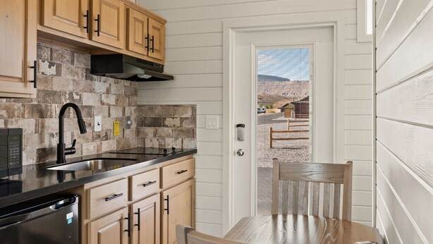 A kitchen with wooden cabinets, a black faucet, and a stone backsplash. - Zion Vacation Cabins (Virgin)