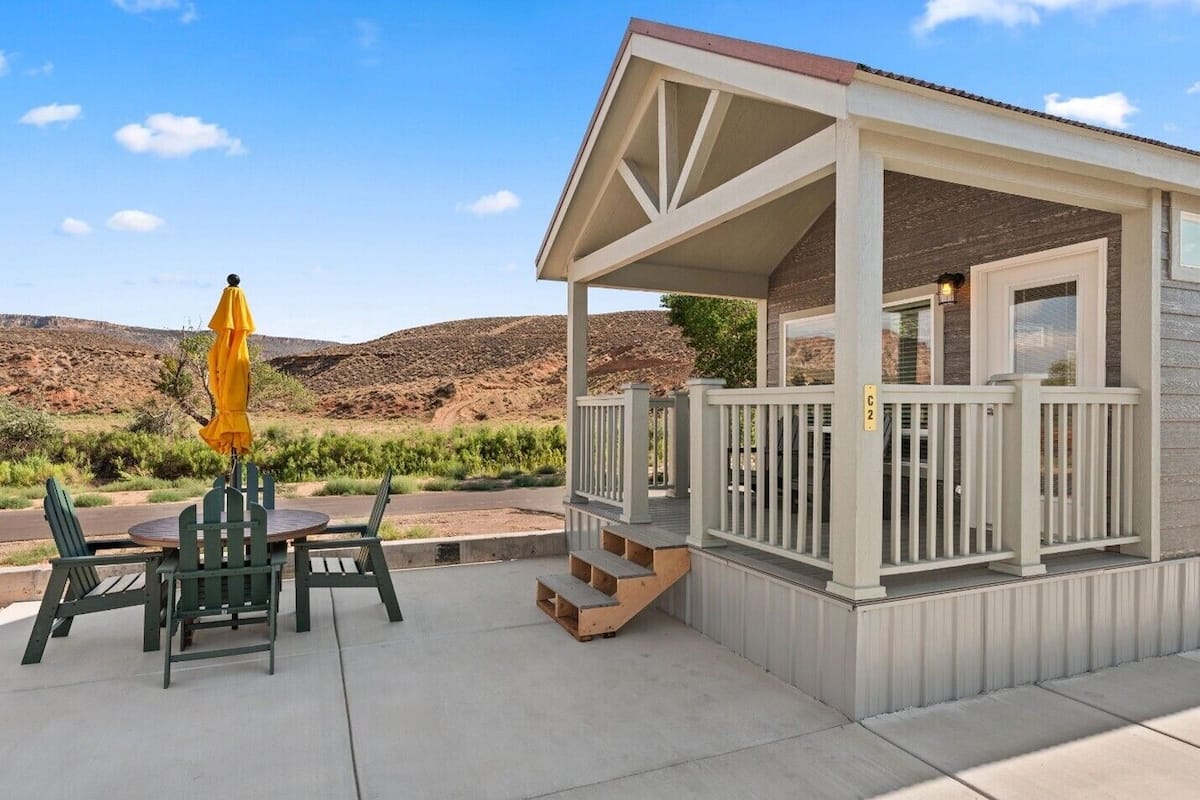 A covered outdoor seating area with a table and chairs, a yellow umbrella, and a view of a desert landscape.