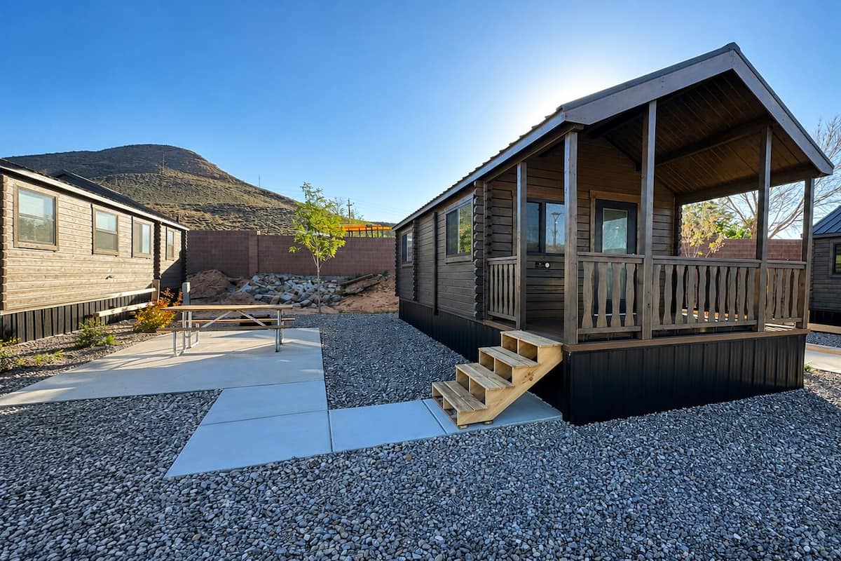 A cabin with a wooden deck, a staircase, and a gravel ground.