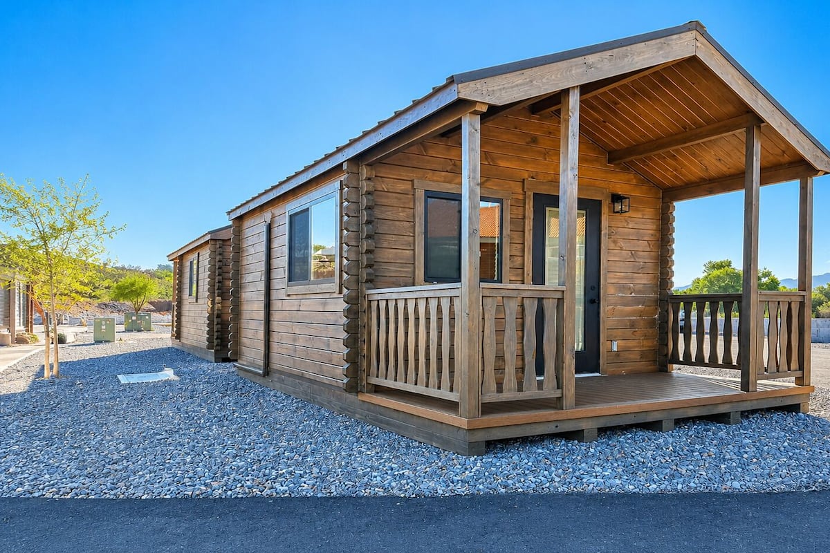 A log cabin with a porch, large windows, and a gravel driveway.