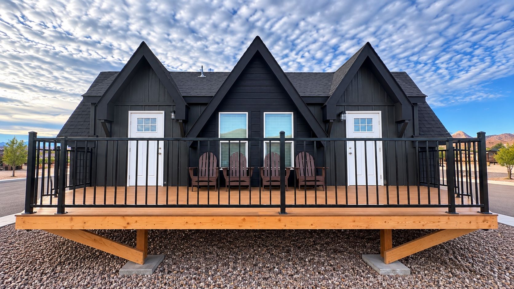 Un edificio a due piani con una terrazza in legno e tre poltrone Adirondack.