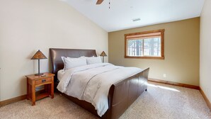 A bedroom with a bed, a nightstand, a lamp, a ceiling fan, and a window. - Exquisite home with mountain views, fireplaces, game room & private Hot tub (Flagstaff)