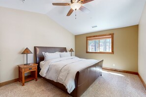 Une chambre à coucher avec un lit, une table de chevet, une lampe, un ventilateur de plafond et une fenêtre.